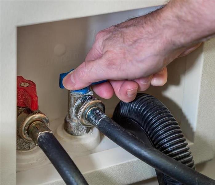 A male hand turns off the cold water valve for a washing machine.