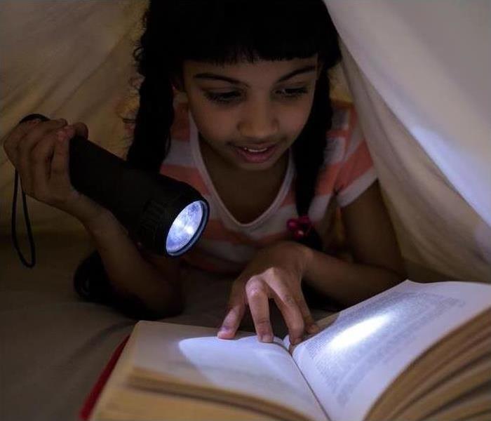A girl uses a flashlight to illuminate a book