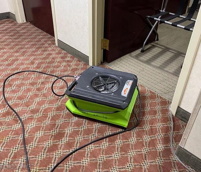 A dehumidifier rests in the open doorway of a hotel room.