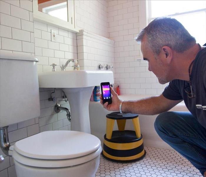 man holding up thermal camera pointed behind a toilet
