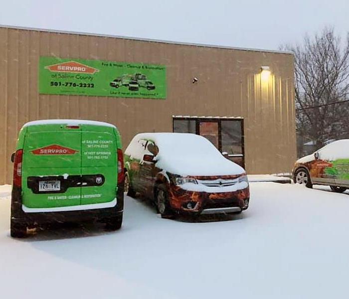 Vehicles are covered in snow in front of a SERVPRO office