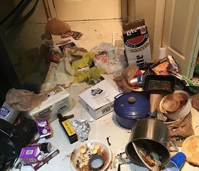 A kitchen floor is covered in trash and old food.