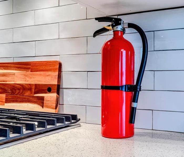 A fire extinguisher sits on a kitchen counter near a stove.