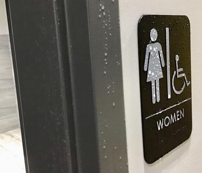 Water drips down a commercial restroom sign
