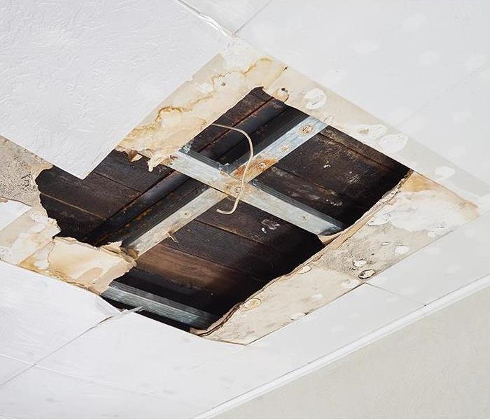 A white ceiling has a large hole as a result of water damage.